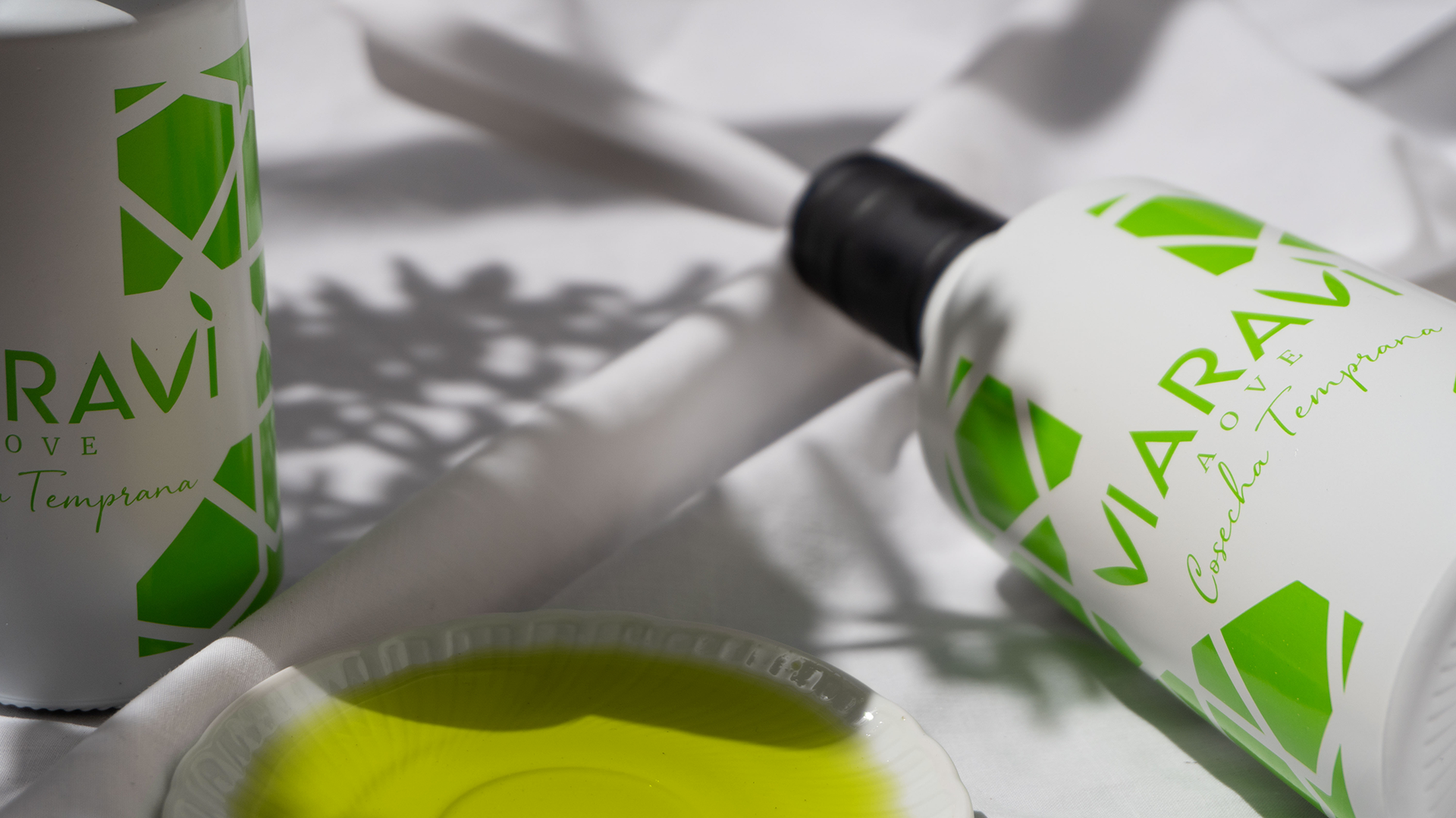 Aceite de oliva virgen extra Viaraví cosecha temprana en botellas blancas y verdes junto a un plato con aceite verde, fotografía de producto